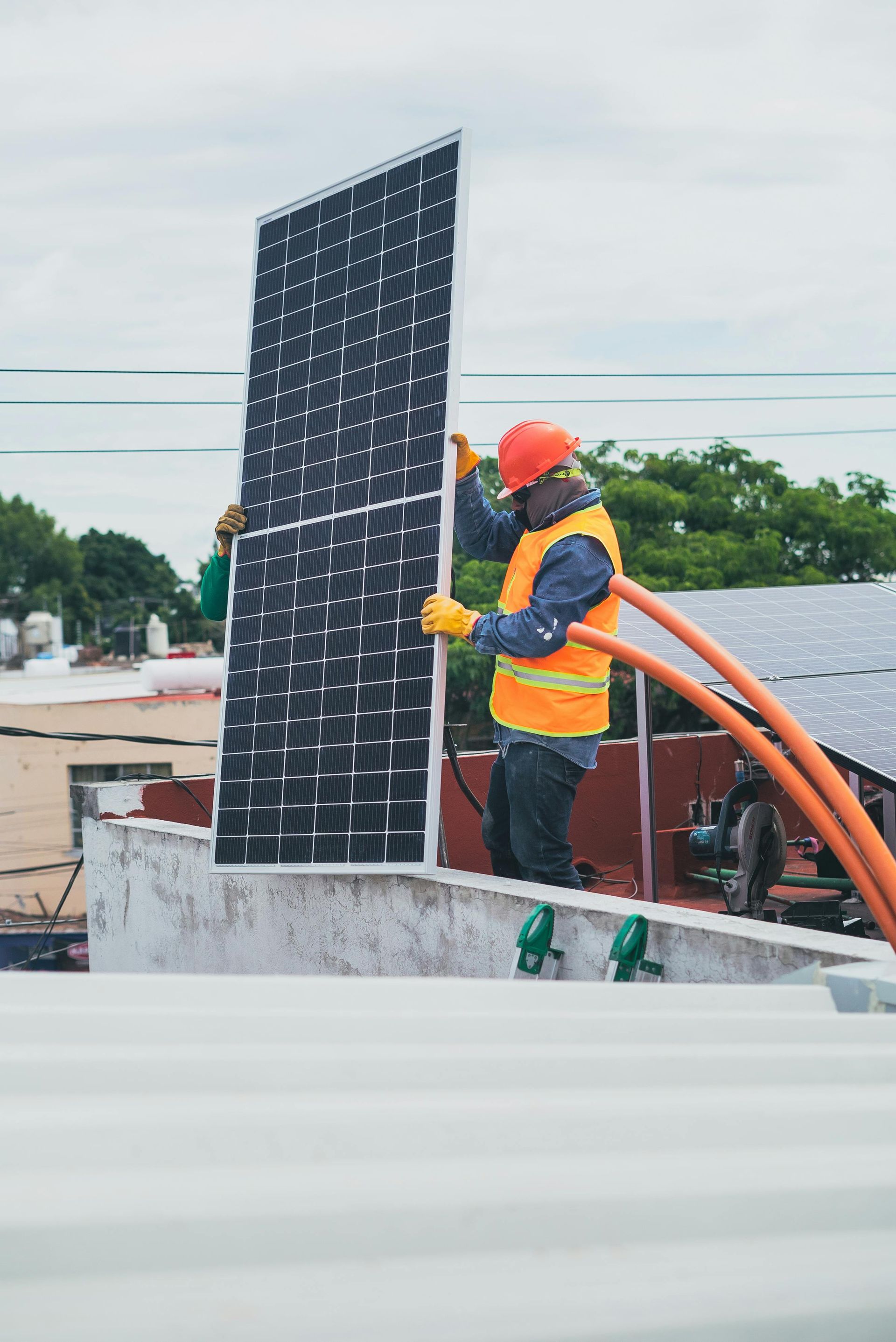 Un obrero de la construcción, con chaleco de seguridad y casco, sostiene un panel solar vertical en una azotea.
