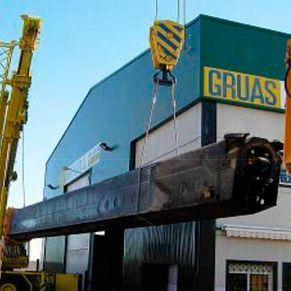 Una gran pieza de metal está siendo levantada por una grúa frente a un edificio.