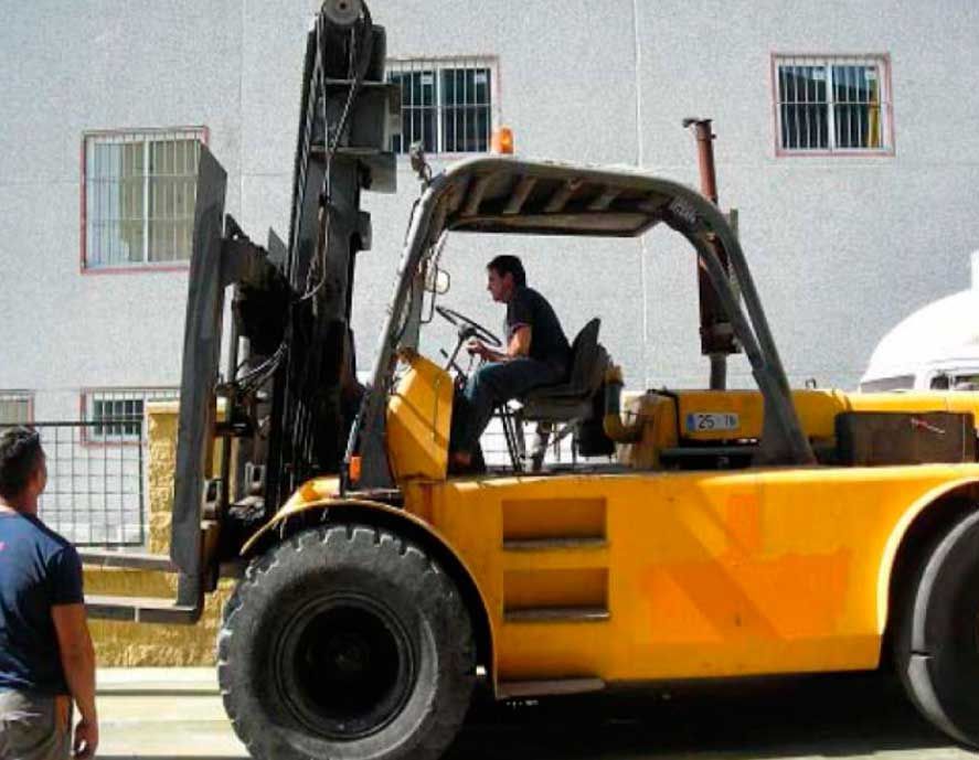 Un hombre conduce una carretilla elevadora amarilla frente a un edificio.
