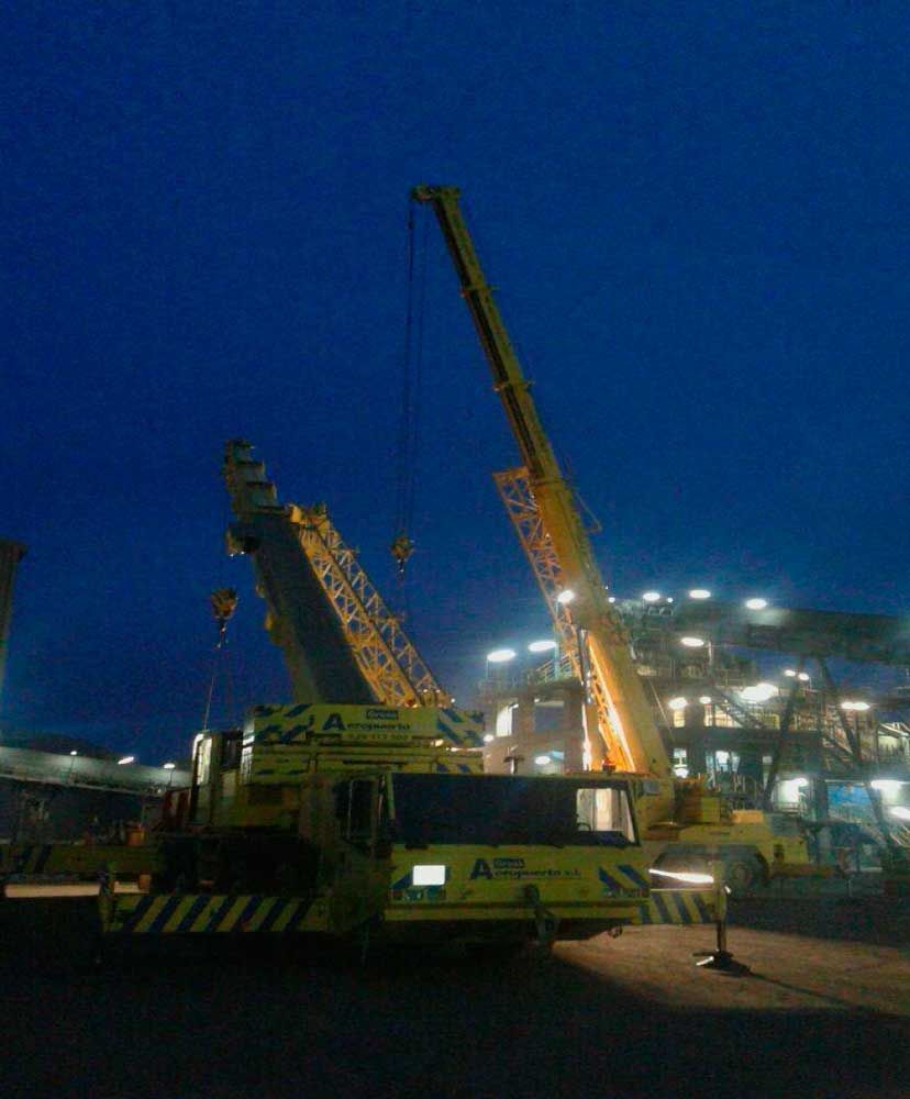 Una gran grúa amarilla está estacionada en un estacionamiento por la noche.