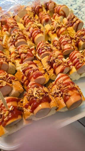 Un montón de perritos calientes en palitos con salsa de tomate y queso en una bandeja.