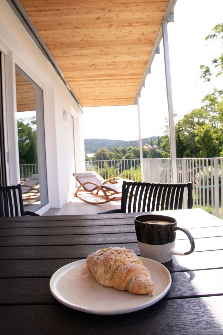 Ein kleines Bett mit brauner und grüner Bettwäsche steht neben einem Tisch mit einer Lampe und einem weißen Sofa.