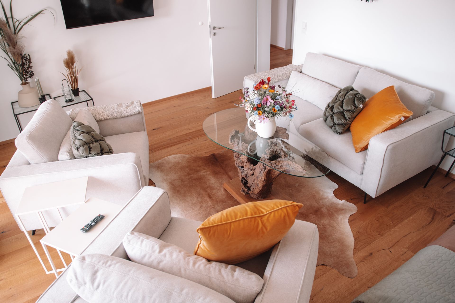 Wohnzimmer mit weißen Sofas, braunem Teppich, Glastisch und bunten Kissen.