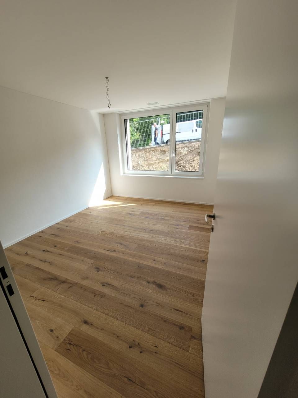 Leerer weisser Raum mit Holzboden und grossem Fenster, das Tageslicht hereinlässt