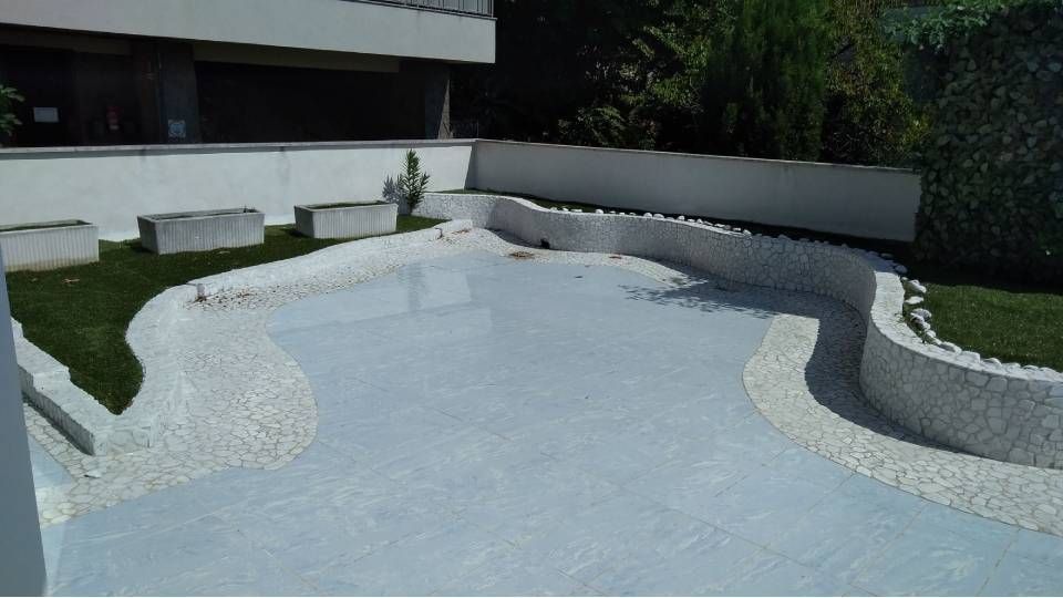 Ein leerer, hellblauer Betonpool mit geschwungenen weissen Stützmauern in einem Innenhof.