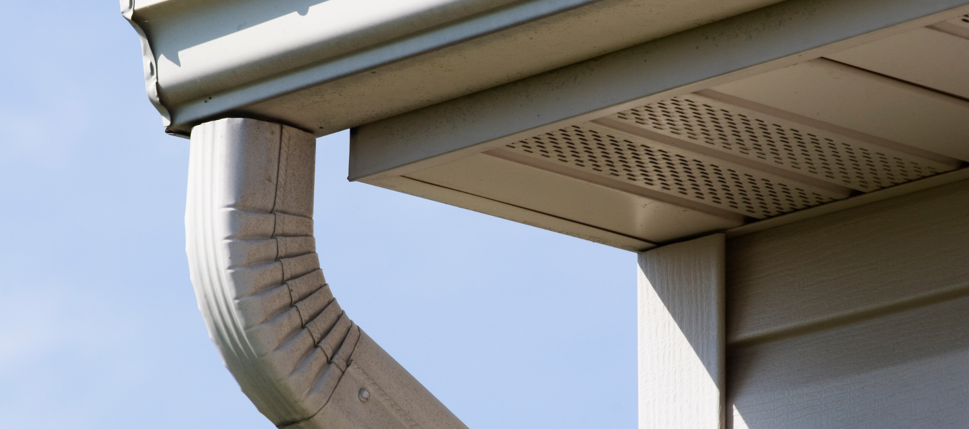 Un système de gouttières sur une maison, incliné vers le bas, avec un ciel bleu clair en arrière-plan.