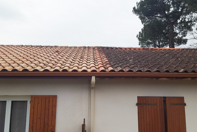 Tuiles de toit en terre cuite à moitié nettoyées, gouttière brune, maison blanche avec volets bruns.