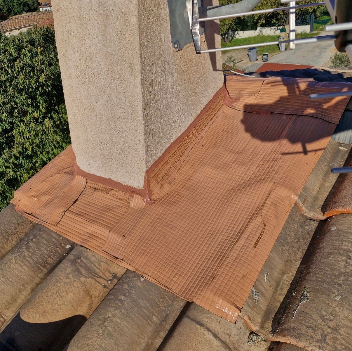 Toiture en tuiles brunes avec base de cheminée recouverte d'un treillis brun rougeâtre, de solins métalliques et de mastic.