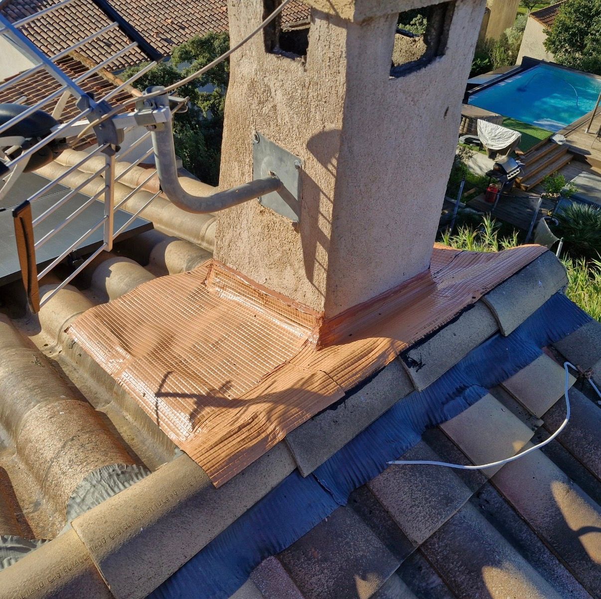 Toiture avec cheminée. Des solins en cuivre entourent la cheminée posée sur des tuiles en terre cuite.