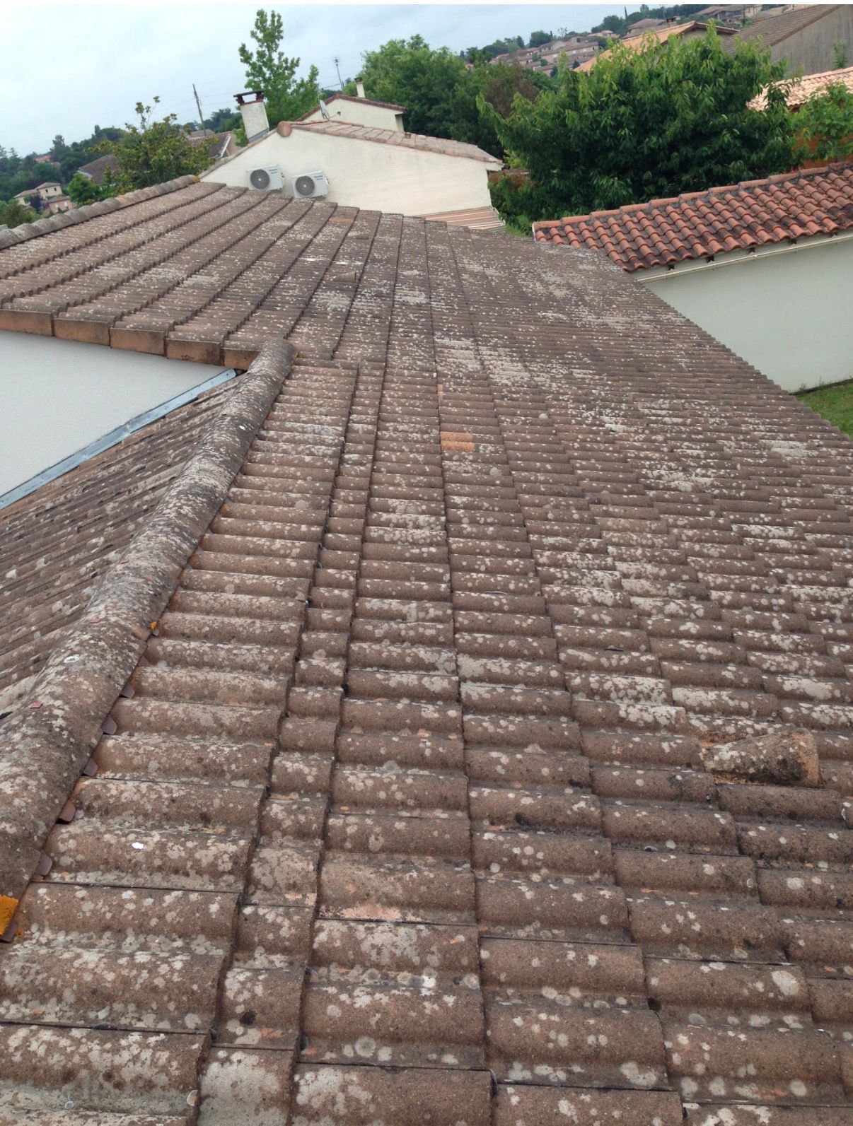 Toit de tuiles en terre cuite recouvert de mousse et de lichen, avec d'autres toits en arrière-plan.