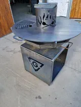 Metallene Feuerstelle für den Außenbereich mit quadratischem Sockel und runder Oberseite auf einem Betonboden