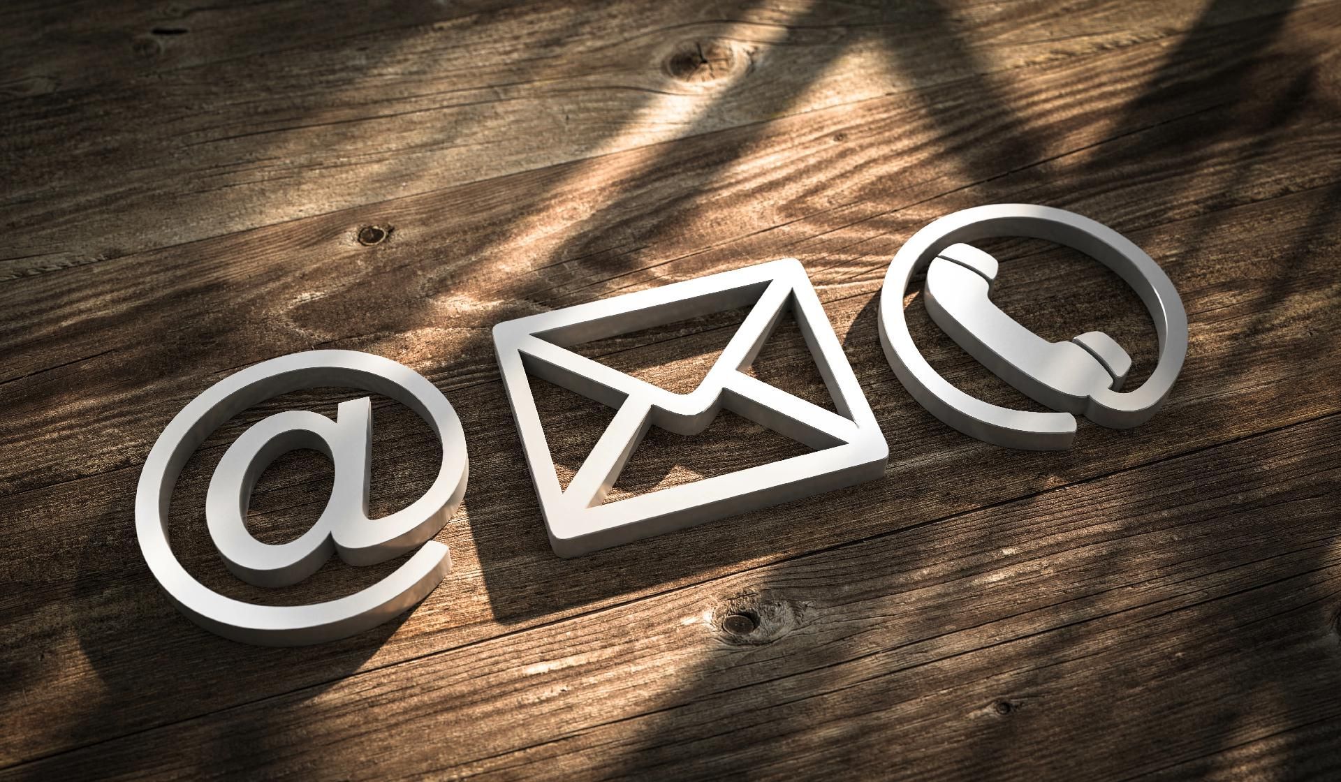 Weiße E-Mail-, @- und Telefonsymbole auf einer Holzoberfläche symbolisieren Kommunikationsmethoden