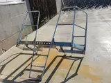 Blauer Metall-Terrassenstuhl, zusammengeklappt auf einer sonnenbeschienenen Betonfläche mit starken Schatten.