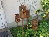 Metallene Gartendekorationen in Katzenform auf Stäben zwischen grünen Pflanzen und gelben Blumen