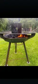 Schwarzer Kugelgrill mit kleinem Feuer in einem grasbewachsenen Hinterhof