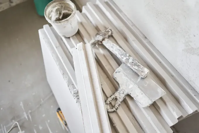 Sobre paneles de construcción blancos, se encuentran herramientas para enlucir, entre las que se incluyen una llana .