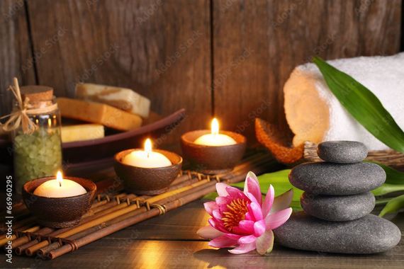 Ambiance spa : bougies allumées, pierres empilées, serviette, fleur de lotus, savon et huile.