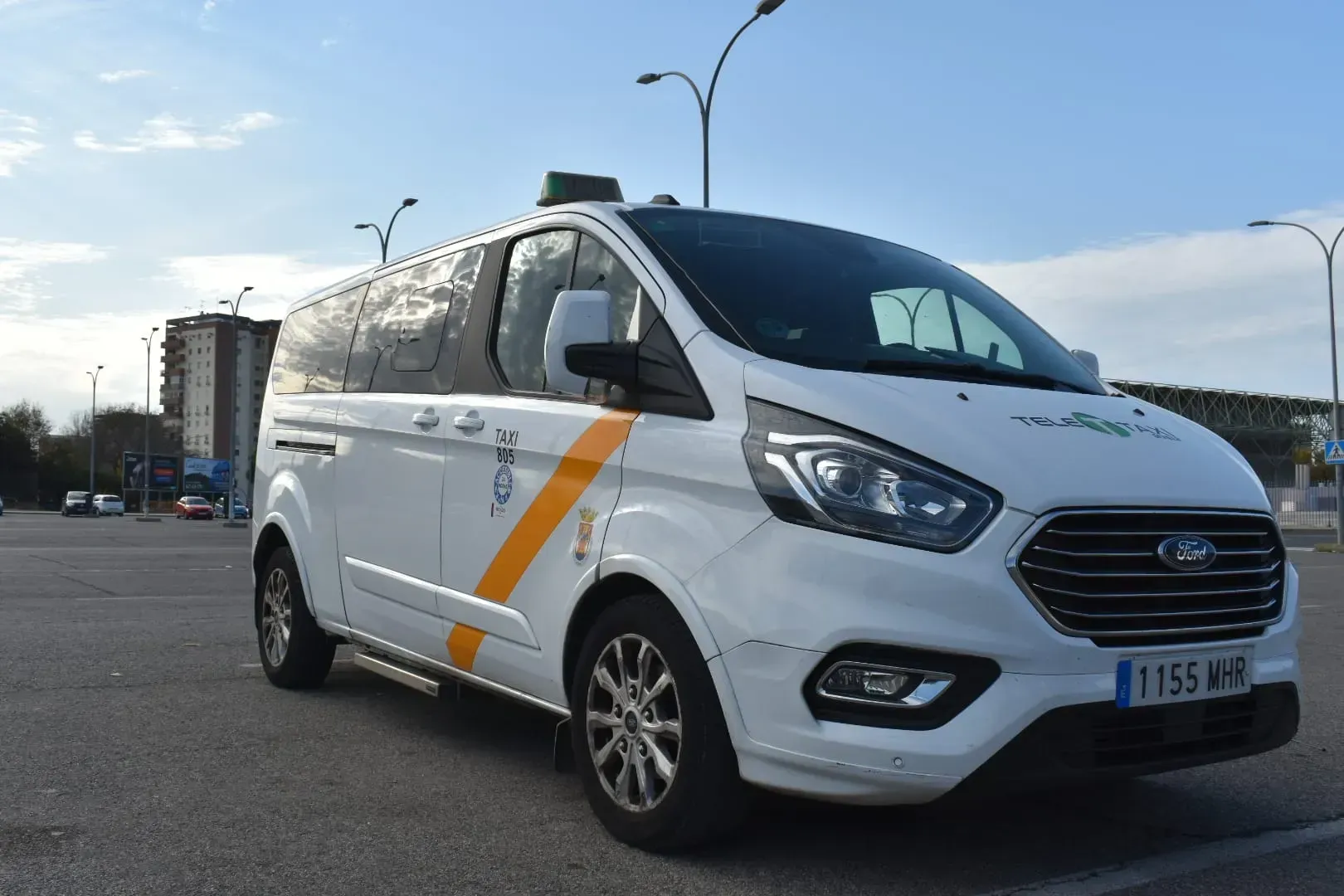 Una camioneta blanca con una franja amarilla en el costado está estacionada en un estacionamiento.