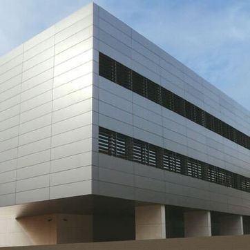Edificio de oficinas moderno de color plata y gris con ventanas horizontales oscuras contra un cielo azul.