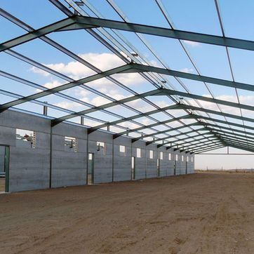 Granero o almacén vacío con estructura metálica en construcción, con paredes de hormigón y suelo de tierra.