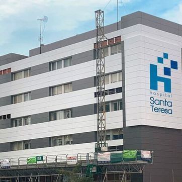 Exterior del Hospital Santa Teresa, un edificio blanco de varias plantas con logotipo azul y antenas en la azotea.
