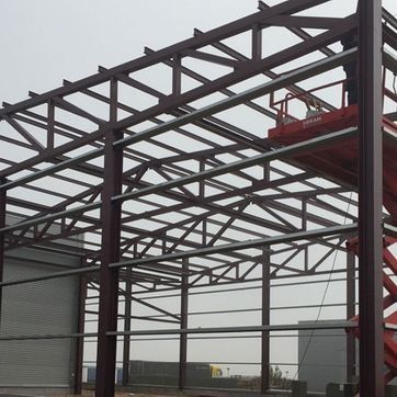 Estructura de acero de un edificio en construcción con una plataforma elevadora roja a la derecha.