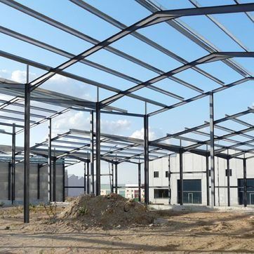Estructura de acero de un gran edificio en construcción con montones de tierra y un cielo despejado.