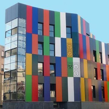 Edificio moderno y colorido con paneles verticales multicolores y una fachada de esquina de vidrio.