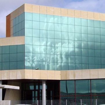 Edificio de oficinas moderno de cristal con detalles en color beige y ventanas azules reflectantes.