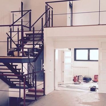Interior de loft moderno con escalera de metal negro y una luminosa habitación sin terminar en proceso de renovación.