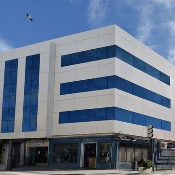 Edificio de oficinas moderno, blanco y azul, en una esquina bajo un cielo despejado.