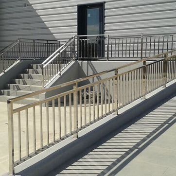 Rampa y escaleras exteriores de hormigón con barandillas metálicas junto a la entrada de un edificio.