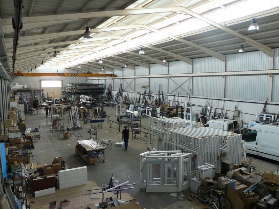Gran almacén industrial con maquinaria, equipos y trabajadores bajo un alto techo metálico.