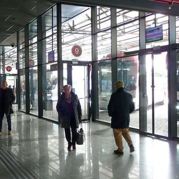 Entrada de cristal a la terminal del aeropuerto con algunas personas caminando y un letrero de la puerta 9 sobre las puertas.
