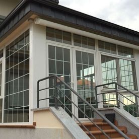 Entrada moderna al edificio con ventanas de cristal, escaleras y barandillas metálicas.
