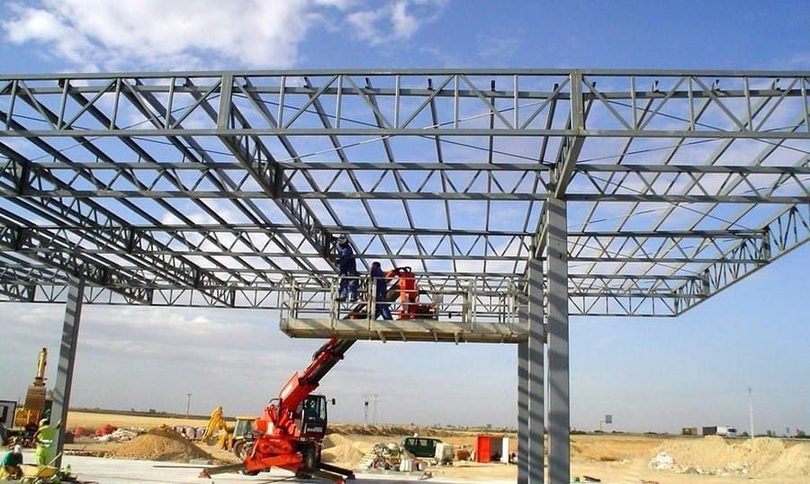 Obreros de la construcción en una plataforma elevadora roja ensamblan la estructura de un edificio de acero al aire libre.
