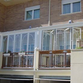 Edificio de apartamentos de ladrillo con balcón acristalado blanco y plantas en macetas.