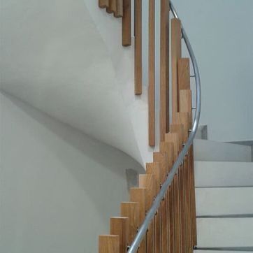 Escalera interior curva con escalones de madera clara y pasamanos de metal sobre paredes blancas.