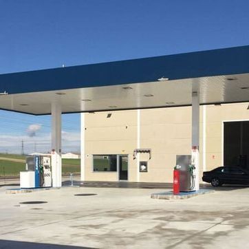 Marquesina de una gasolinera con surtidores en un día soleado, techo azul y un coche negro aparcado.
