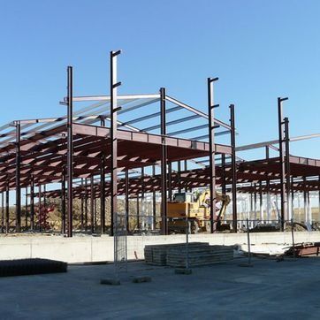 Estructura de acero de un edificio en construcción sobre una base de hormigón bajo un cielo azul despejado.