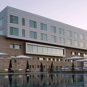 Exterior de hotel moderno con fachada en la azotea y patio junto a la piscina al atardecer.