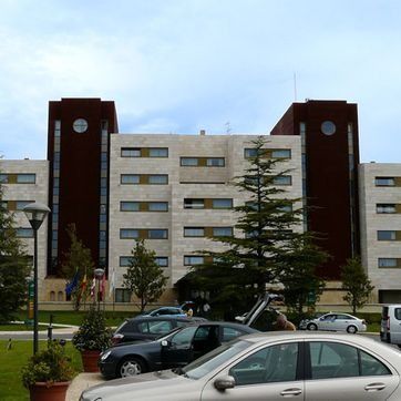 Edificio de apartamentos moderno con coches aparcados y árboles delante bajo un cielo nublado.