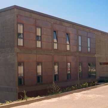Edificio de ladrillo de dos plantas con ventanas altas junto a una carretera pavimentada en pendiente bajo un cielo azul.