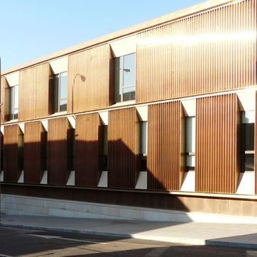 Fachada de edificio moderno con listones de madera verticales y ventanas altas que reciben una cálida luz solar.