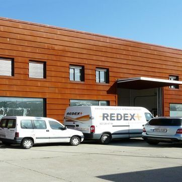 Almacén moderno de color naranja con furgonetas de reparto aparcadas delante.