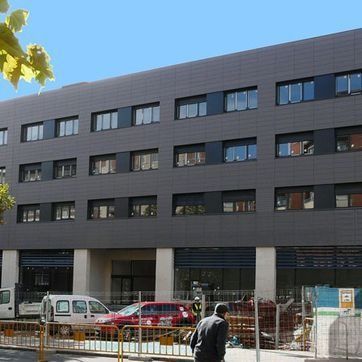 Edificio de apartamentos moderno de color gris oscuro con furgonetas aparcadas y una valla de construcción delante.