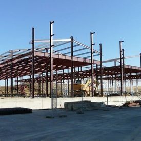 Estructura de acero en construcción sobre un terreno de hormigón bajo un cielo azul despejado.