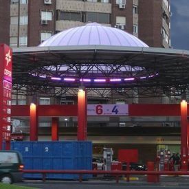 Entrada a un edificio moderno con una cúpula iluminada de color púrpura y un letrero con el número 6-4 sobre columnas rojas.
