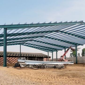 Estructura de acero en construcción con vigas color turquesa y una grúa en un terreno baldío.