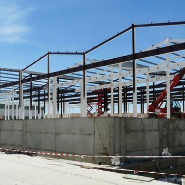Edificio con estructura de acero en construcción, con cimientos de hormigón y cielo azul.